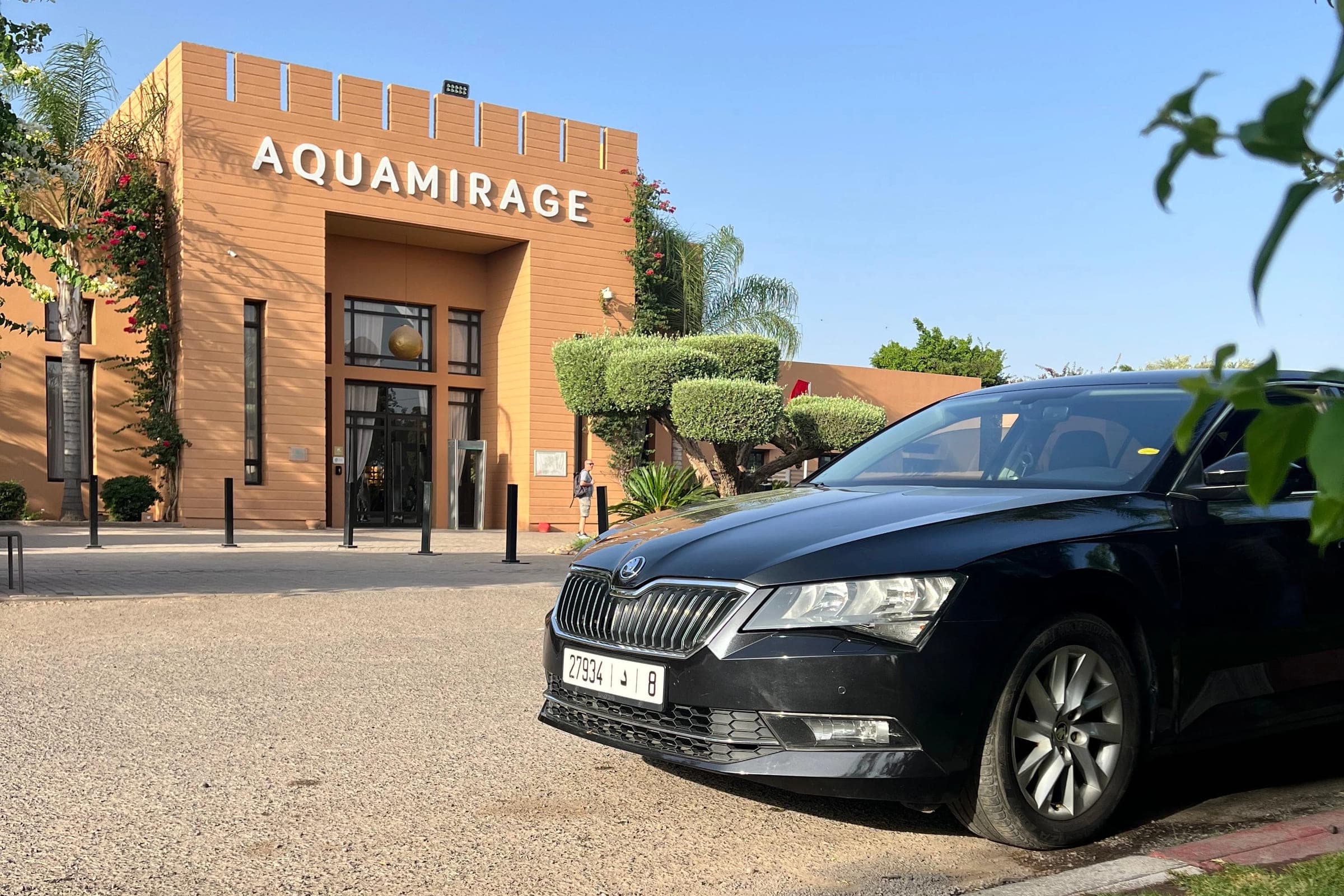 A black Škoda Superb standing at a hotel entrance under a clear sky