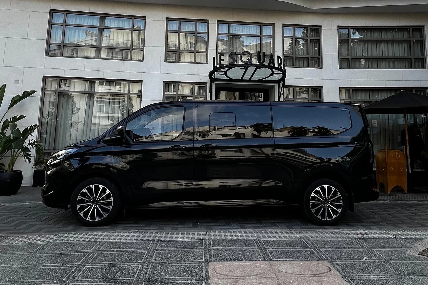 Black Ford Tourneo seen in profile, stopped outside a hotel entrance