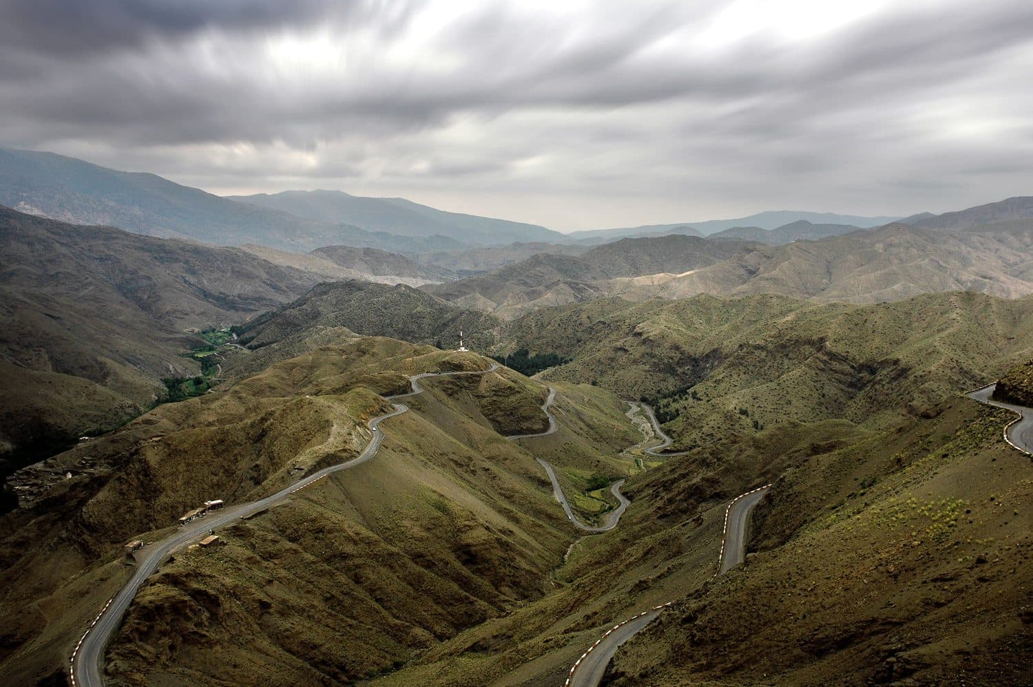 Winding road crossing the green Atlas hills under an overcast sky
